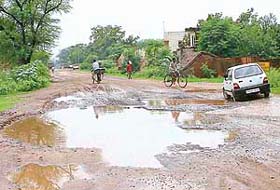 A car driver avoids a deep pothole on the Mubarikpur-Ramgarh road in Daffarpur village