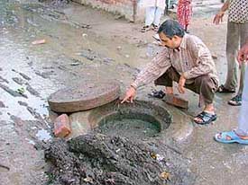 A resident shows a choked sewer manhole in the Gulabi Bagh area
