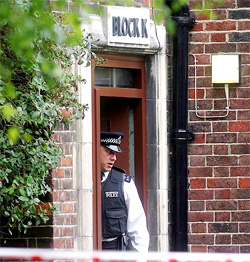 A police officer looks out from the entrance to Block K on the Peabody estate in Dalgarno Gardens, following arrests at the property in connection with bomb attacks on the city, in west London on Sunday