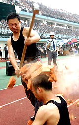 A Chinese security personnel breaks bricks placed on his colleague's head with a hammer during a security protection skills show at a stadium in Chengdu