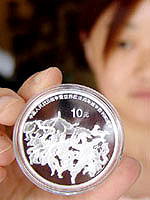 A Chinese woman shows a silver coin minted to commemorate the 60th anniversary of Japans defeat in World War II at a coin trade company in Zhengzhou in China on Monday.