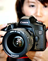 An employee of Japan's camera giant, Canon, displays a new 35mm full-frame digital SLR camera, EOS-5D, equipped with a 12.8 mega-pixel CMOS sensor and a large 2.5-inch LCD display on its back, at the company's showroom in Tokyo