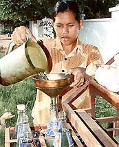 A woman fills recycled soft drink bottles with petrol for sale at a roadside shop on the outskirts of Phnom Penh
