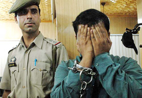 Sumit Arora of Chandigarh, an employee of a private mobile service provider, hides his face as the police presents him before mediapersons in Srinagar on Sunday.
