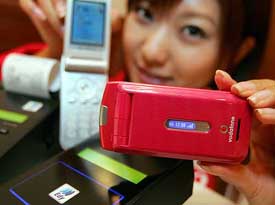 A model holds a Vodafone KKs new 3G handset 703SHf over a card reader as she demonstrates how the handset can be used as a reader-equipped cash register to make payments, during an unveiling event in Tokyo on Tuesday
