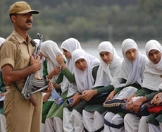 A security jawan stands guard while schoolchildren watch an air show of the Indian Air Force (IAF) where Suryakiran jet trainers leave a trail of colours over the Dal Lake in Srinagar on Thursday.