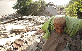 An earthquake survivor carries supplies as he walks past destroyed houses at Mujhoi village, 17 km from Muzaffarabad, capital of Pakistan-occupied Kashmir, on Monday