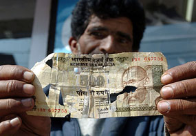 Izhar, a money changer, poses with a crumbling Rs 500 note for exchange at his market stall in Srinagar on Monday. 