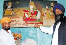 Sarpanch Ranjit Singh Bhala (right) shows a painting depicting Maharaja Ranjit Singh changing the village name from Bura to Bhala. 