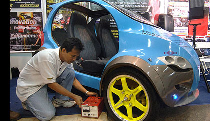 An exhibitor checks the battery charger near a display of an electric car made by Filipino company, Castech