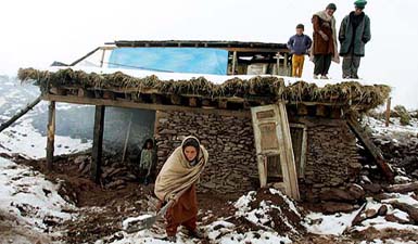 An earthquake survivor cleans snow from the front of her shelter in the devastated village of Pieer Chanasi, about 25 km east of Muzaffarabad, on Sunday