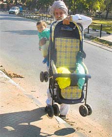 AGE NO BURDEN: Well aware of the traffic hazards on Chandigarh roads, an old man thinks it prudent to carry the child and his pram to cross the road