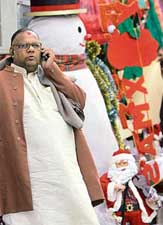 A passerby talks on his mobile phone next to a giant styrofoam snowman and a Santa Claus doll at a market in New Delhi.