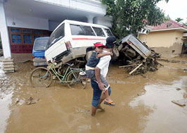 A man carries his son and walks past damaged cars and houses in the flooded village of Rambi Puji, near the town of Jember, East Java, on Monday.