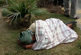 A man sleeping on a roundabout in the city squeezes into his small sheet