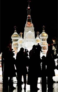 People are silhouetted in front of a 16-foot-high ice sculpture