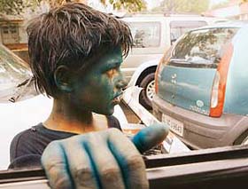 A boy, with his face painted with colour, sells newspapers at a traffic intersection in New Delhi