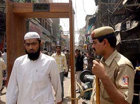 A devout watched by a policeman as he walks through a metal detector outside the Jama Masjid in New Delhi