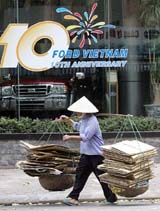 A woman carrying used boxes for recycling walks past a showroom of US automaker Ford bearing a sign marking its 10th anniversary of operations at Hanoi on Monday