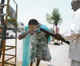 A man helps a woman quench thirst during a hot day in Ludhiana on Thursday