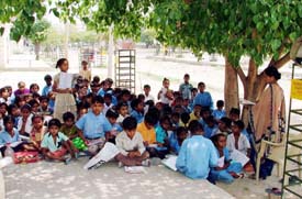 Children sit on a concrete platform under a tree at a school in Rishi Nagar in Ludhiana