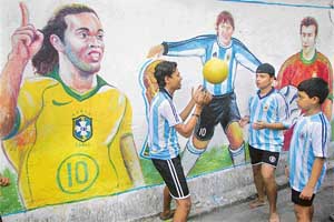 Boys play beside a wall adorned with images of football stars in Kolkata.