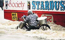 A man pushes a bicycle as a bus passes by along a flooded road after a heavy rainfall in Mumbai