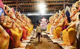 A boy walks past rows of Ganesh idols carrying food for artisans busy making the idols for the forthcoming Ganesh Festival in Mumbai on Friday