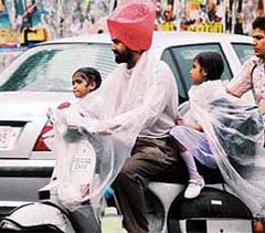 A man uses polythene sheets to shield himself and his two daughters from rain on Wednesday afternoon in Ludhiana.