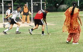 A hockey match being played on a ground having pits and overgrown grass