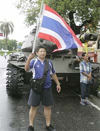 A man waves a Thai national flag in front of a tank outside Government House in Bangkok