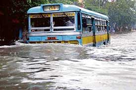 A bus carrying passengers makes its way through a waterlogged street in Kolkata 