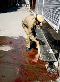 A policeman washes blood near the spot of a grenade attack by militants on a Kashmir police vehicle in Srinagar