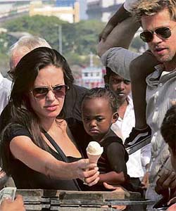 Hollywood star Angelina Jolie carries adopted daughter Zahara while buying an ice cream cone as Brad Pitt watches outside their hotel in Mumbai