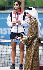 A ceremony official walks past silver medallist Sania Mirza during the award ceremony for the womens singles tennis final in Doha on Wednesday. 