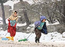 Children pull water containers as it snows in Kabul on Sunday.