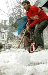 A shopkeeper removes snow from outside his shop before starting the daily business in Shimla on Thursday.