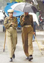 CRPF personnel take shelter under an umbrella to save themselves from rain at Jantar Mantar in the Capital on Wednesday