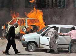 A lawyer walks past judicial staff trying to move a car while another burns during clashes in Lahore on Saturday. 