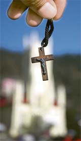 A devotee holds aloft a Jesus Christ locket with the church at the Ridge in the background on the eve of Good Friday in Shimla on Thursday