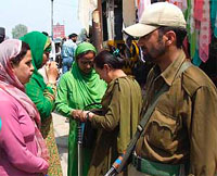 A security jawan guards as a policewoman checks Kashmiri women during a search operation in Srinagar on Friday.