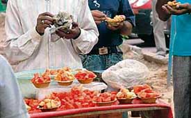 A vendor sells cut fruit exposed to flies and dust near