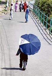 With the mercury shooting up to 25.1C in the state capital during the day, a school student seeks cover under an umbrella on his way back home on Thursday