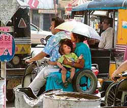 A family finds respite from the scorching Sun under an umbrella on a busy road in Ludhiana.