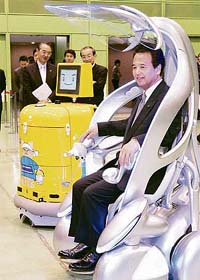 Japanese trade and industry minister Akira Amari (right) sits inside Toyota's iUnit, a next generation personal vehicle, at a photo session with Fuji Heavy Industry and Sumitomo Corp's cleaning robot in Tokyo