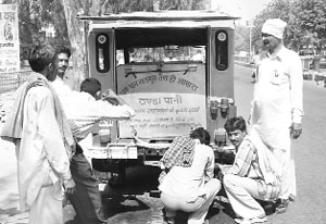 Sri Kishen Sharma of Hisar (wearing a white turban) looks on as passersby quench their thirst from the water tank he has fitted in his jeep.