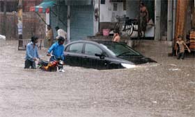 People watch a car half submerged in flood water after the heavy rain