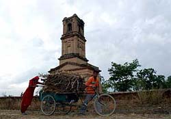 A man carries dry wood as his wife pushes the rickshaw from behind in the backdrop of a church tower at Karnal.
