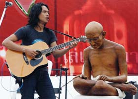 A musician plays music next to a statue of Mahatma Gandhi during an anti-coup rally near Bangkok's Grand Palace