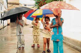 Children enjoy rain under the cover of colourful umbrellas in Mandi Ahmedgarh